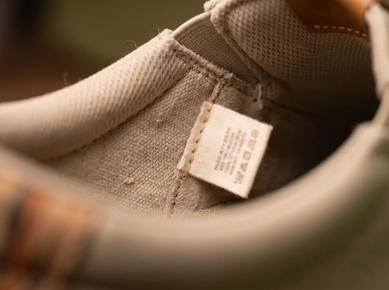 Close-up of a small woven care label sewn inside the heel of a canvas shoe, its print out of focus