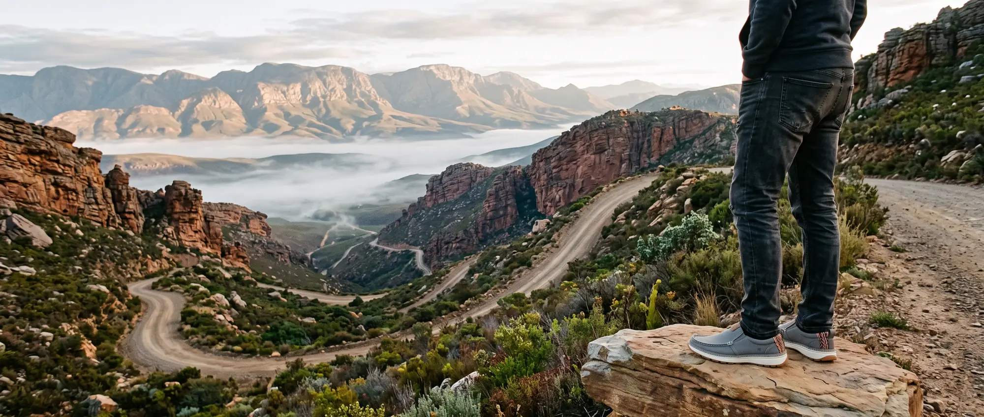 A gravel switchback road through red sandstone cliffs in the Swartberg at sunrise, mist in the valley